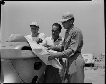 Three men looking at map spread out on nose of Piper Cub