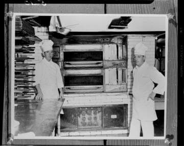 Two chefs standing by electric bake ovens in a commercial kitchen
