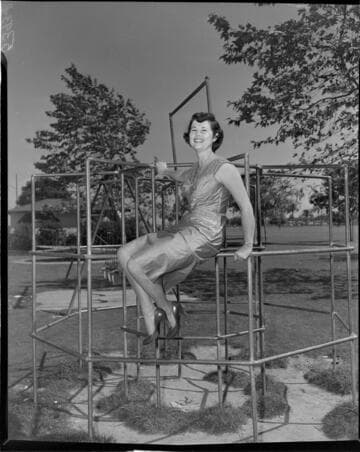 Young lady in a dress and high heals sitting in monkey bars at park playground