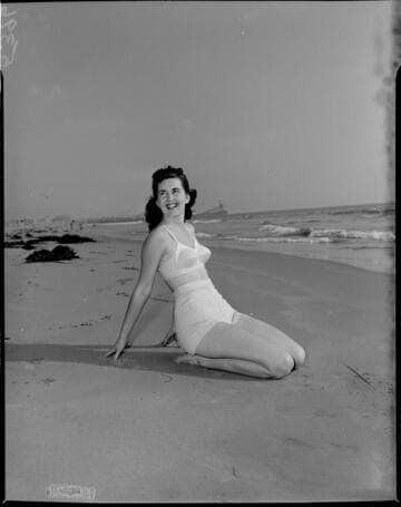 Young lady in 50s bikini kneeling on the sand