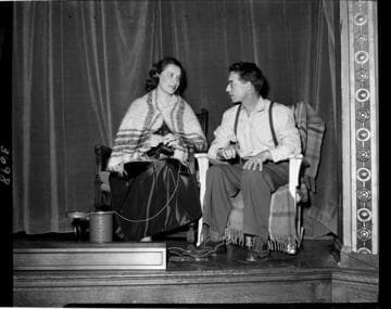 Performance of skit at Edison auditorium.  Man and woman in rocking chairs.  Woman has a shawl and is knitting