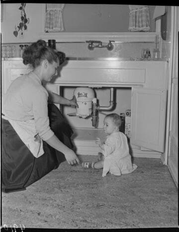 Mother with her baby on the floor looking at garbage disposal under sink