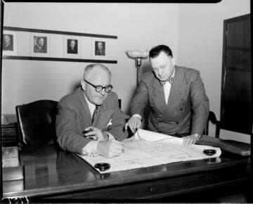 Two men going over plot plans on desk