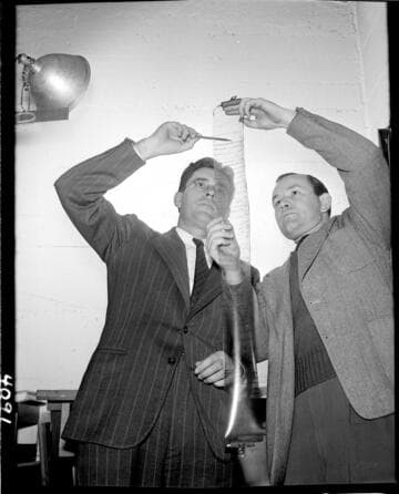 Two men looking at data plots on a roll of film they're holding up to the light