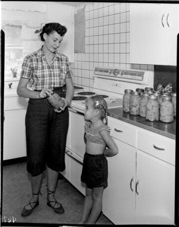 Woman with her little girl in kitchen canning peaches