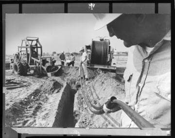 Linemen laying underground electric cables into trench