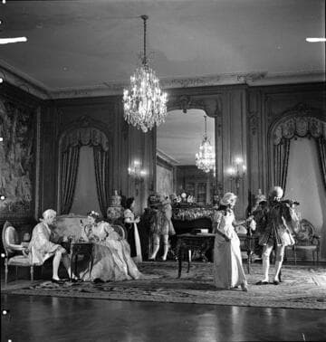 Six people in period costume in the east end of the library of the Huntington residence