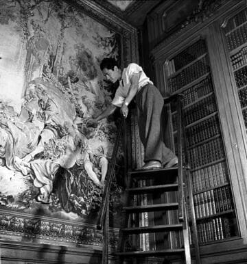 Attendant dusting Beauvais tapestry, "The Flute Player," in the library of the Huntington residence