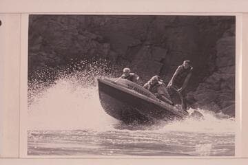 The "Rattlesnake" in Mile 217 Rapid, Grand Canyon. Joe Desloge is at the left, Rod Sanderson is the pilot and Hugh Cutler is in back of him. Argwen Bundy stands on the after deck bracing against a rope bridle
