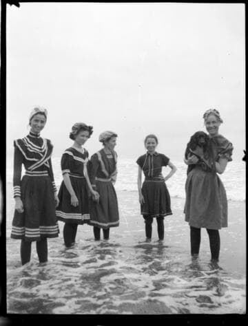 A group of five young women standing in the water at the beach