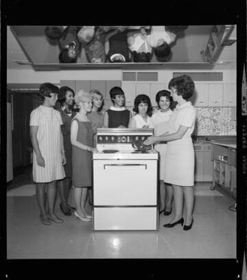 Home economist giving a demonstration on electric appliances to group of ladies in a teaching kitchen