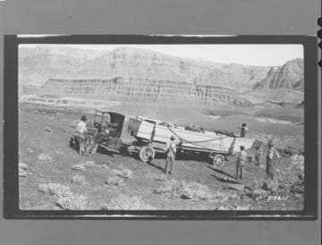 Seven men with truck and trailer carrying one of the Colorado River Expedition boats clearing a path for the rig to get down to the Colorado River
