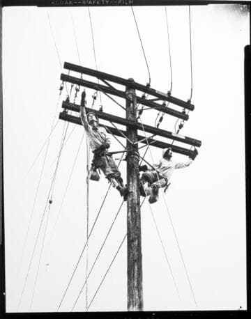 Two linemen working in harness at the top of a double-circuit pole