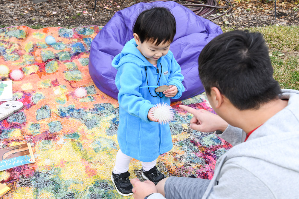 A child and an adult stand on a blanket in a garden.