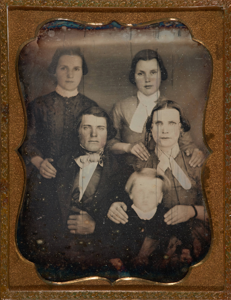 A sepia tone image of a family of five in a gold-tone frame.