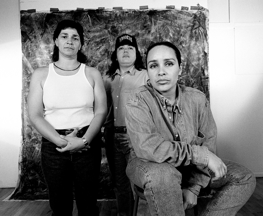 Laura Aguilar, #4, from the series Plush Pony, 1992 Group of three queer women posing for a portrait in front of a roughly textured backdrop