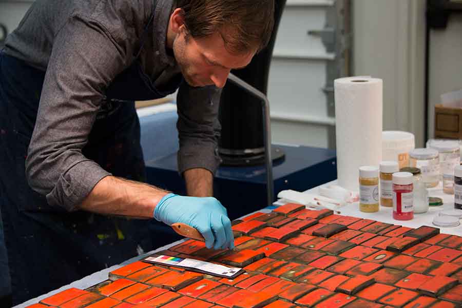 In this photograph, MacLean uses an artist knife to apply a thin coat of a treatment comprising acetone, Paraloid B-72 (a clear acrylic resin), marble powder, and dry pigment to a damaged section of a tile. In this photograph, MacLean uses an artist knife to apply a thin coat of a treatment comprising acetone, Paraloid B-72 (a clear acrylic resin), marble powder, and dry pigment to a damaged section of a tile.