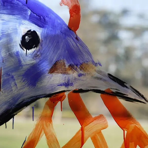 Close up of a bird's head and beak painted on glass with trees and lawn blurred in the background.