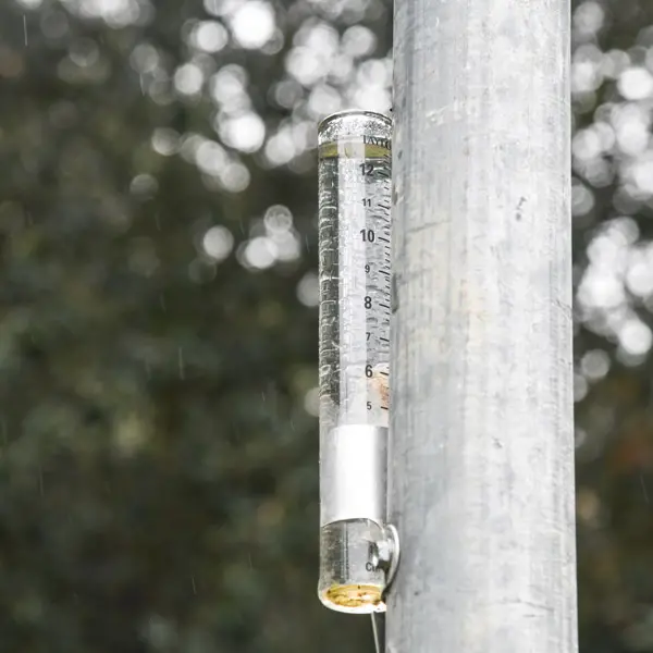 A rain gauge attached to a metal pole.