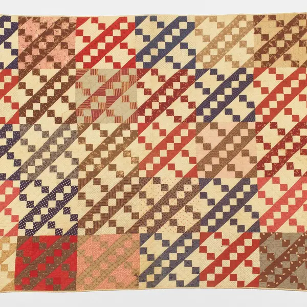 Quilt with Jacob’s Ladder pattern in red, pink, cream, tan, and brown.