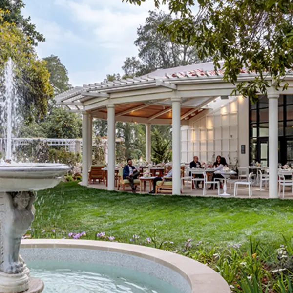A large garden fountain stands in front of an open pavilion dining area.