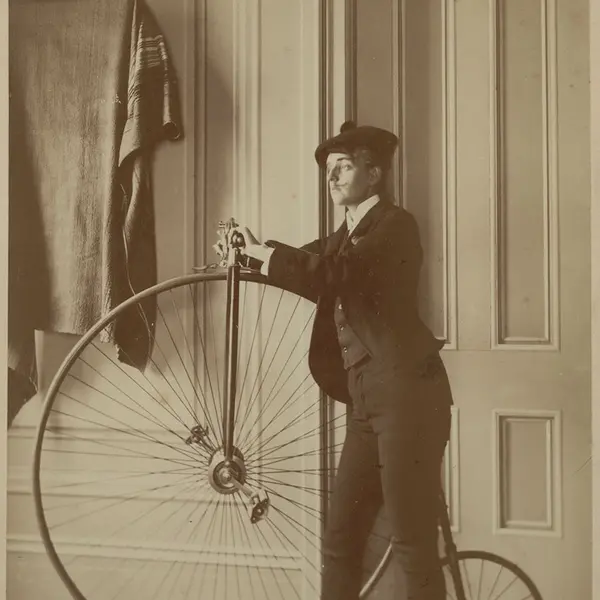 Black-and-white photo of Frances B. Johnston dressed in a suit, posing with a penny-farthing.