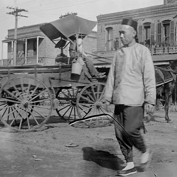 Photograph of an Asian person walking in front of a hose-drawn wagon in Los Angeles' Old Chinatown, circa 1900.
