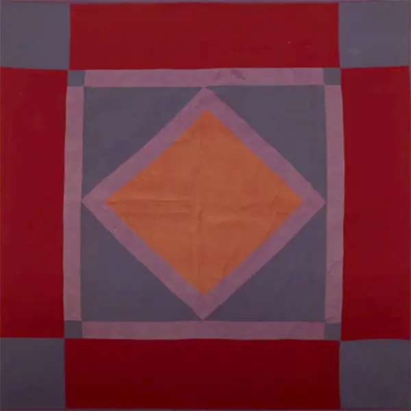 A quilt with squares of blue, rectangles of red, and an orange diamond in the middle.