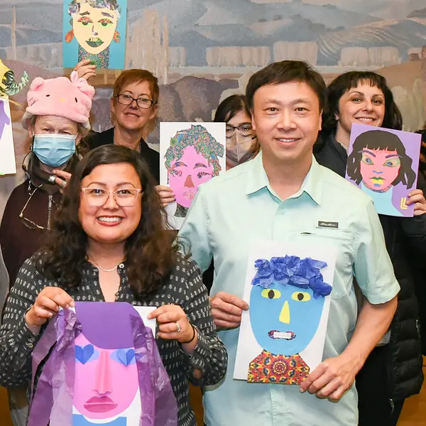 A group of adults stands with self-portraits made from cut paper.