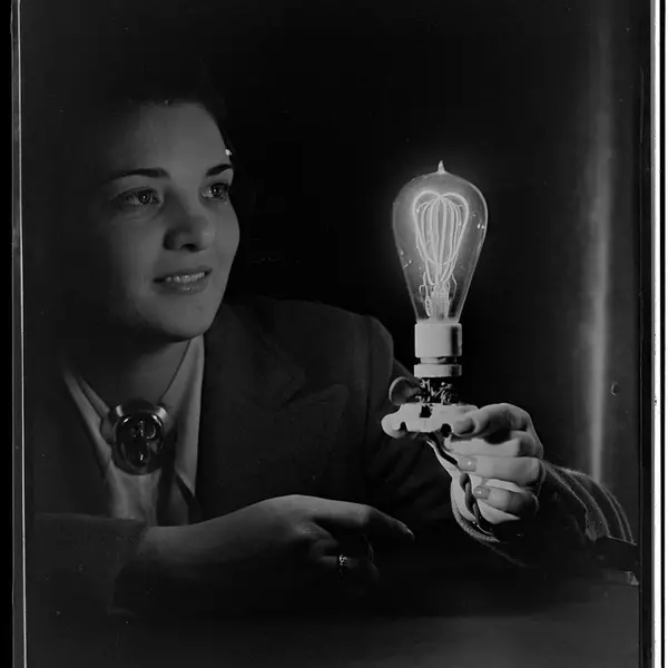 Black and white photo of a person looking in wonderment at a lit up lightbulb in her hand.