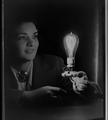 Black and white photo of a person looking in wonderment at a lit up lightbulb in her hand.