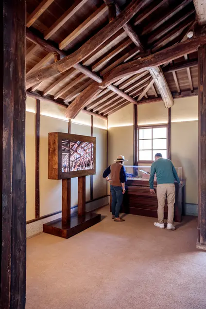 Visitors look at a display case inside a traditional Japanese home with an exposed wood-beam ceiling.