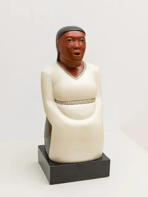 Wood figure of a woman in a white dress with a belt around her waist.
