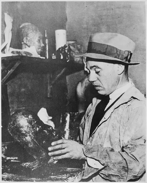 Black-and-white photo of Sargent Claude Johnson in a jacket, tie, and hat, holding an art piece.