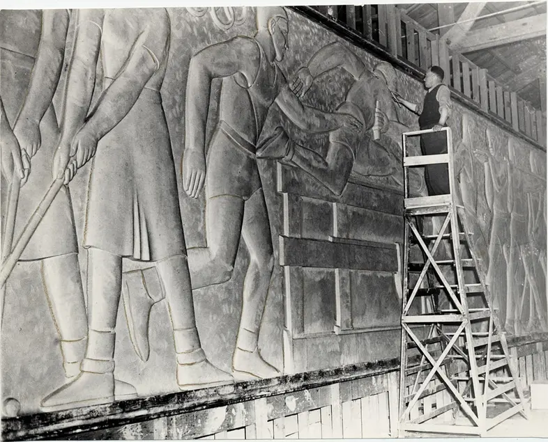 Sargent Claude Johnson stands on a tall ladder in front of a massive wall sculpture.