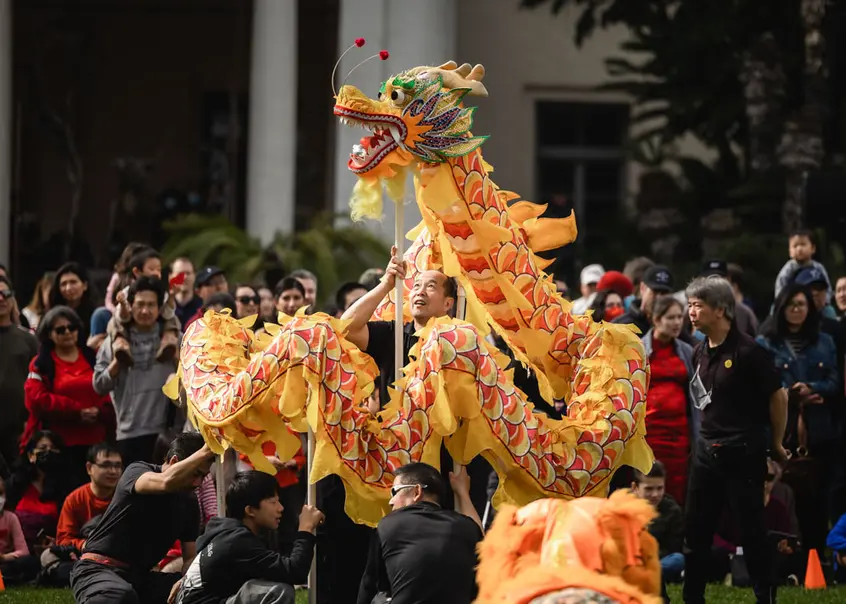 A crowd of people watch a yellow dragon puppet.