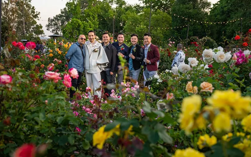 A group of six people pose for the camera surrounded by blooming roses.