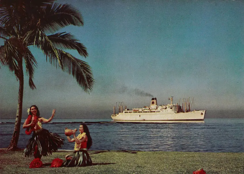 Two people in Hawaiian dress perform on a lawn near the ocean, with a white ship in the distance.