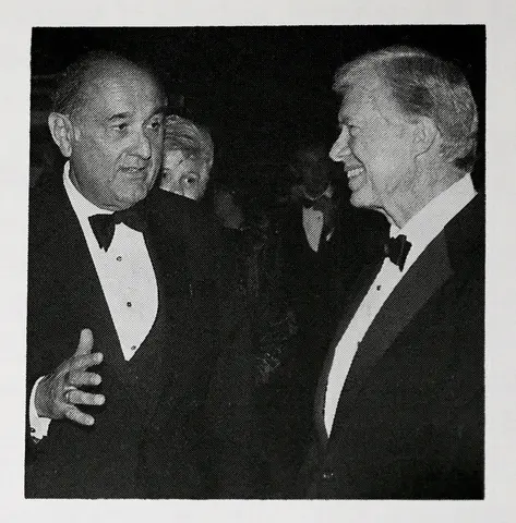 Two men dressed in tuxedos and bowties talk to each other.