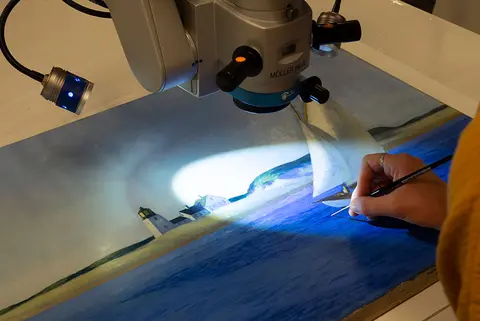 A microscope light illuminates a section of painting.