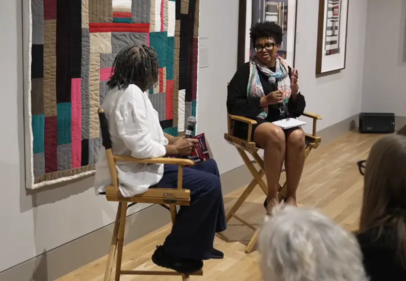 two women sitting in chairs having a conversation in a gallery