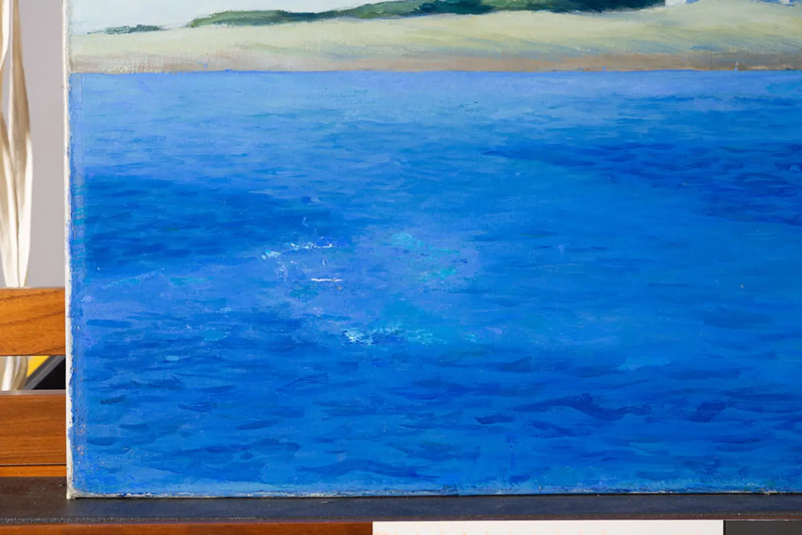 A section of a painting that shows blue ocean water with a shore of land in the background.