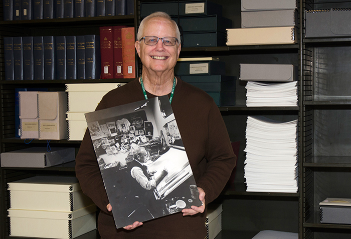 Dennis Harbach, volunteer at The Huntington, holds an image of the cartoonist Paul Conrad at his drawing board. Harbach produced searchable metadata for the satirical cartoons in the Paul Conrad papers. Photo by Lisa Blackburn.