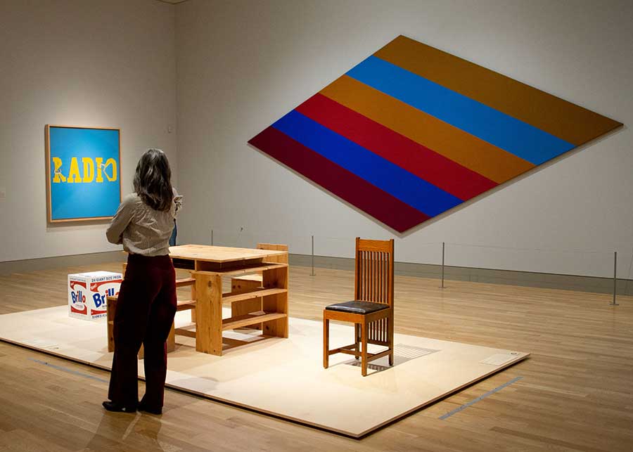 A new arrangement in the Virginia Steele Scott Galleries of American Art features a Brillo Box by Andy Warhol and furniture by Frank Lloyd Wright and Donald Judd. All three artists used the rectangle to achieve stripped-down, straightforward works that, when placed side-by-side, reveal how complex, personal, and historically contingent “simplicity” can be. In the background are Ed Ruscha’s Radio (1964) and Kenneth Noland’s Par Transit (1964). Photo by Deborah Miller.